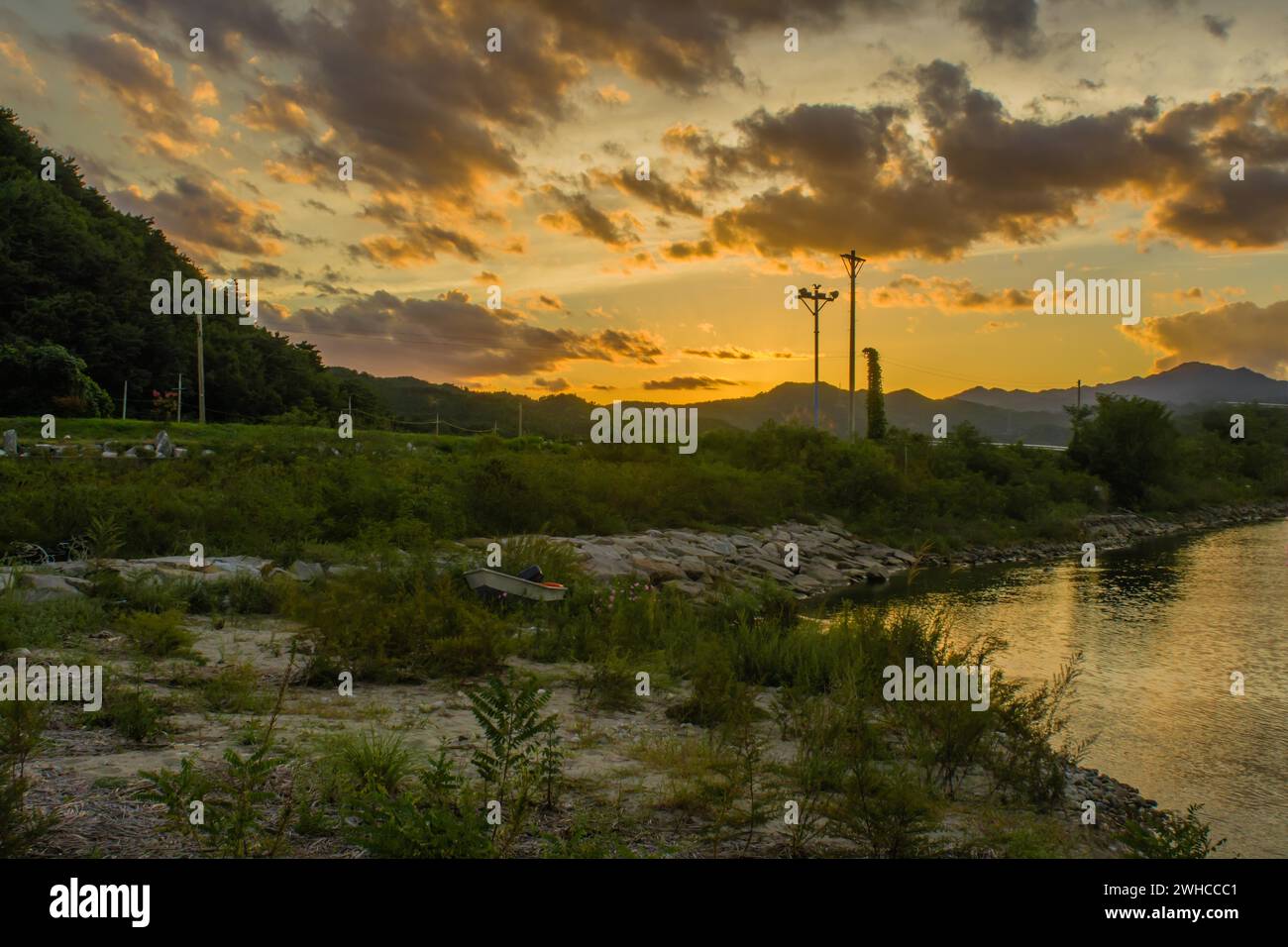 Landscape of beautiful sunset with puffy clouds in sky over inlet shore with a small fishing boat on shore next to waters edge in South Korea Stock Photo