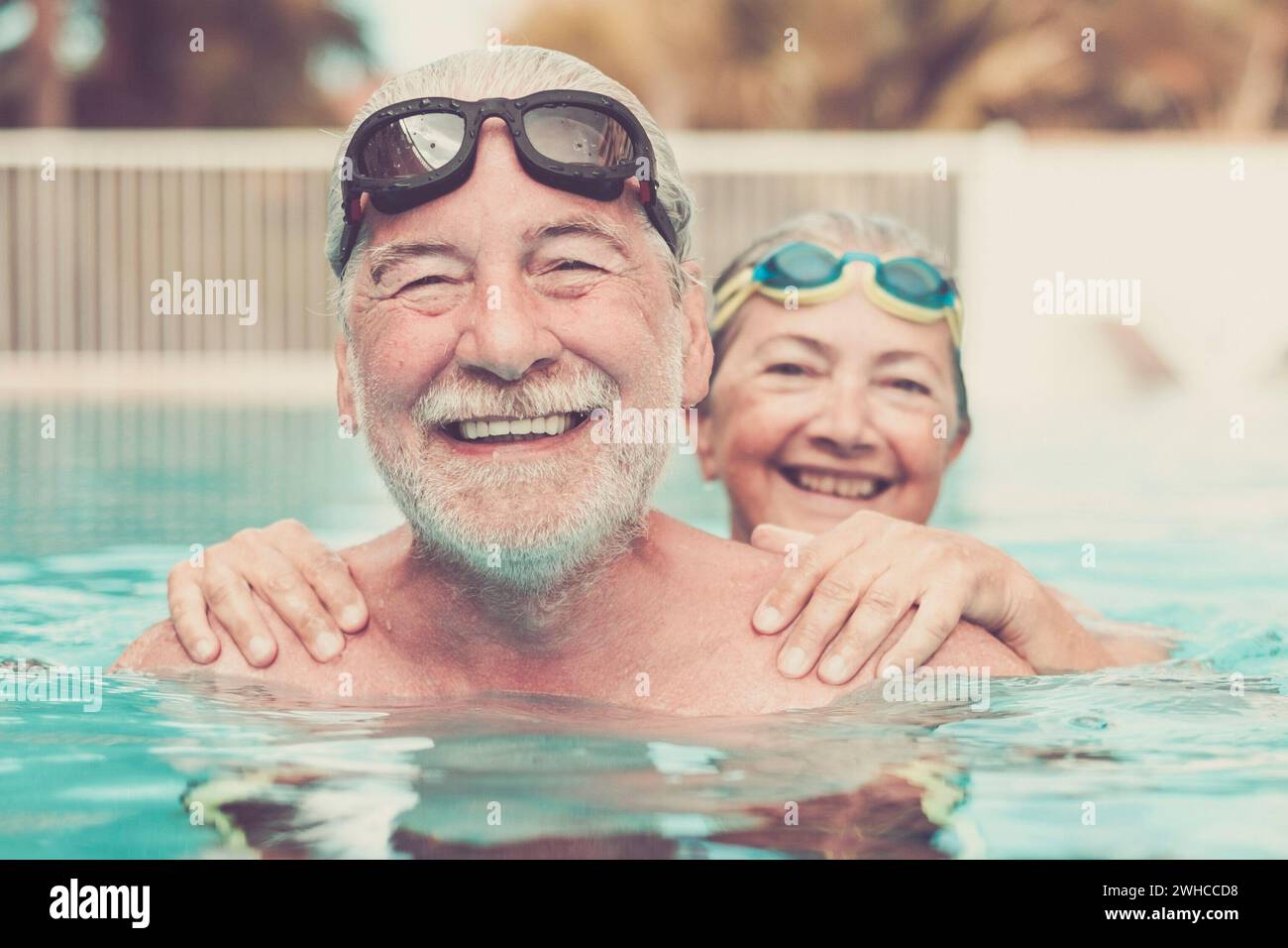 two seniors at the pool hugged together and playing - happy mature people and couple of pensioners looking at the camera smiling Stock Photo