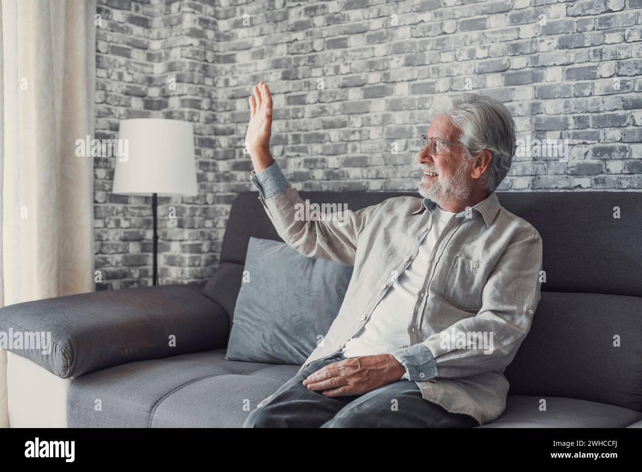 Portrait of happy mature 80s man sit on couch at home look at window posing relaxing on weekend, smiling positive senior 70s grandfather rest on sofa at home or retirement house, show optimism Stock Photo