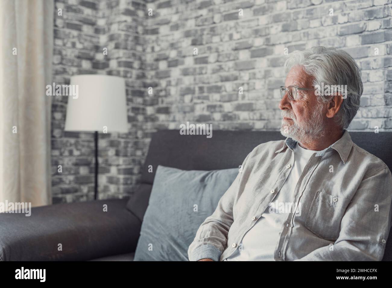 Face of senior caucasian hoary man looking away deep in sad thoughts feels lonely close up portrait, recollect memories and life moments, depressed grandfather alone indoors, yearning for wife concept Stock Photo