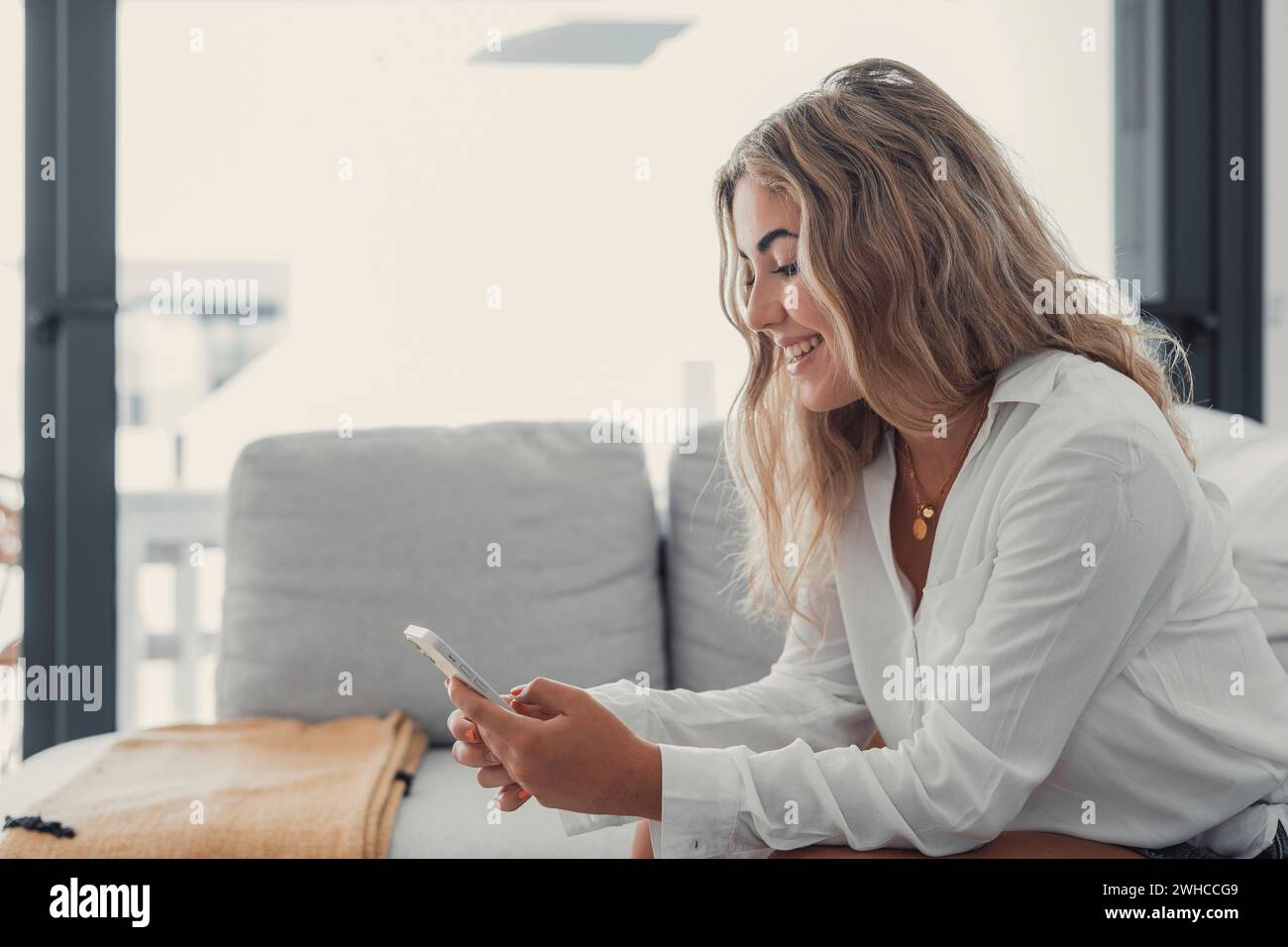 Portrait of one young attractive blonde woman using phone cell on couch relaxing surfing the net at home. Relaxing online concept lifestyle Stock Photo