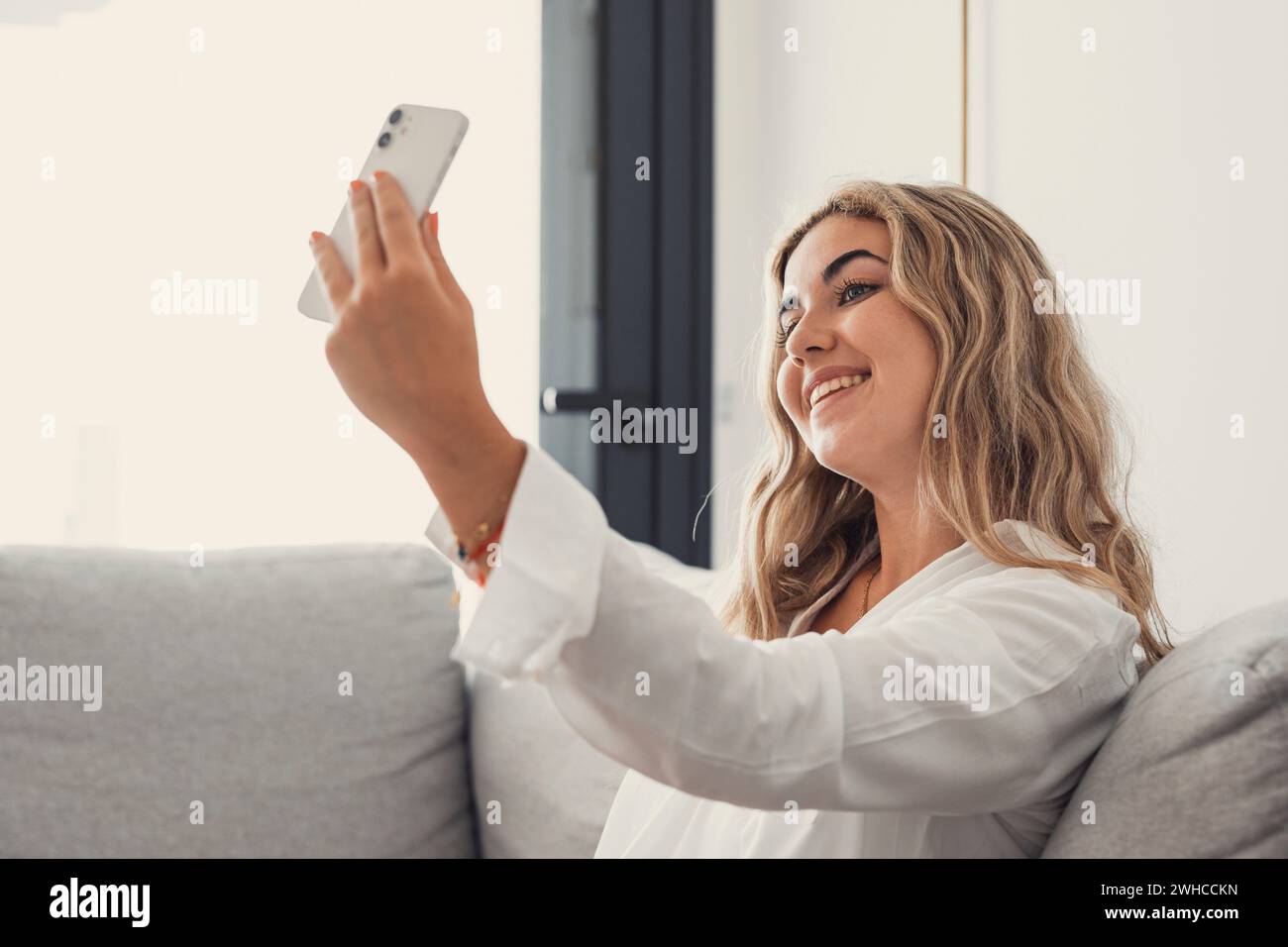 Selfie picture of happy beautiful young woman looking at camera with toothy smile. Pretty girl holding gadget with webcam, making video call, self home portrait. Communication concept Stock Photo