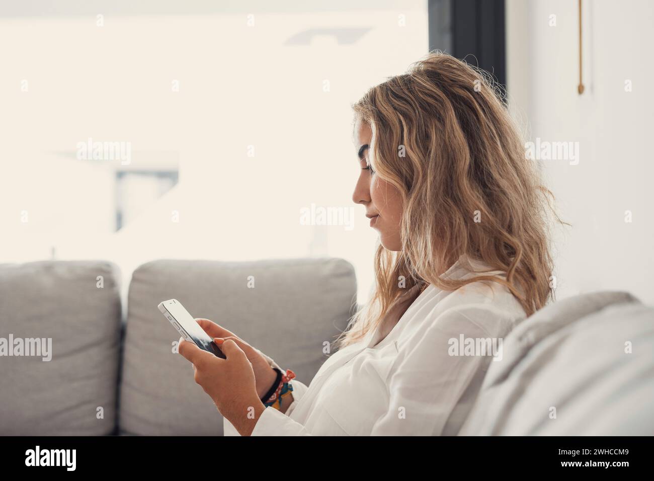 Portrait of one young attractive blonde woman using phone cell on couch relaxing surfing the net at home. Relaxing online concept lifestyle Stock Photo