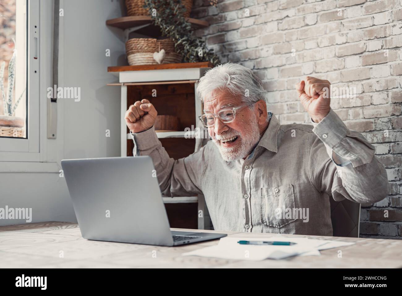 Happy excited old elderly man winner excited by reading good news looking at laptop, overjoyed senior mature grandfather watching game online celebrating goal bid bet win great result victory concept Stock Photo