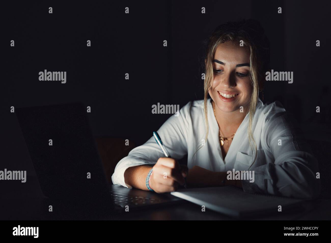 Close up smiling confident caucasian student using laptop at night in office, working, finishing project at late hours, deadline, looking at computer screen, sitting at desk for university homework Stock Photo