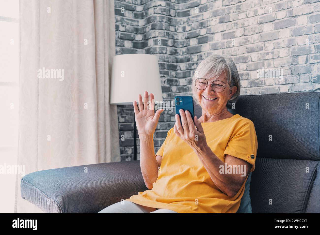 Happy elderly lady talking on cellphone, making call from home, speaking to family on mobile phone with toothy smile. Senior 70s woman consulting doctor on cellphone, chatting to friend, laughing Stock Photo