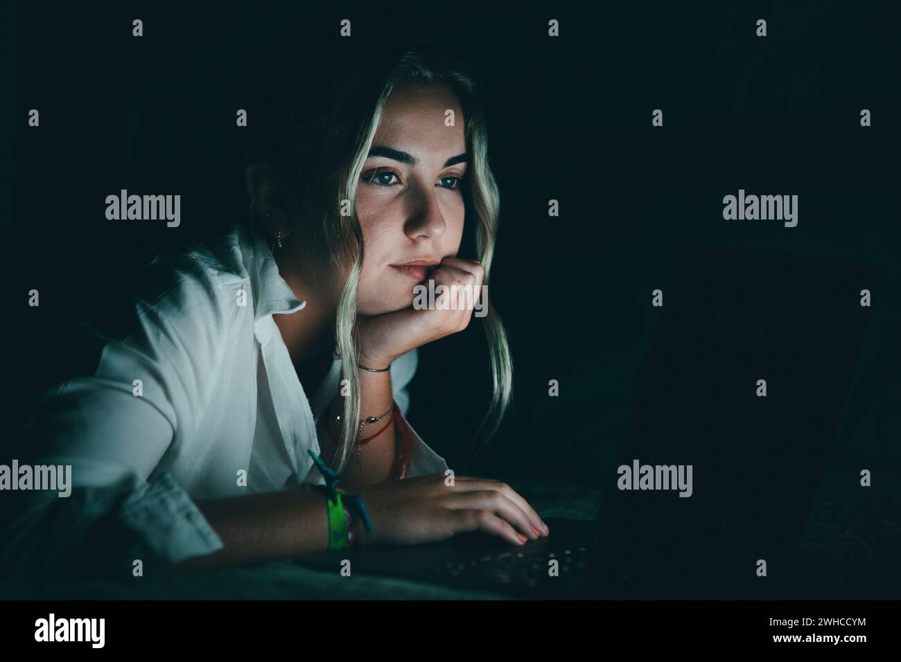 Close up serious confident caucasian student using laptop at night in bed, working, finishing project at late hours, deadline, looking at computer screen, sitting at bedroom for university homework Stock Photo