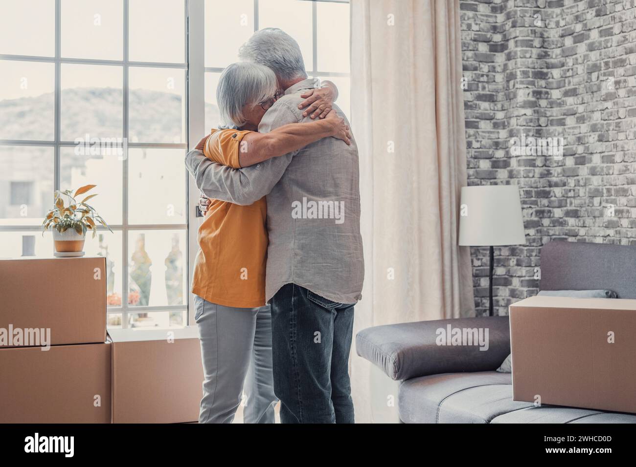 Happy grateful elder wife embracing husband with love, affection in at stacked cardboard boxes in new apartment, celebrating real estate property buying, moving into new home Stock Photo