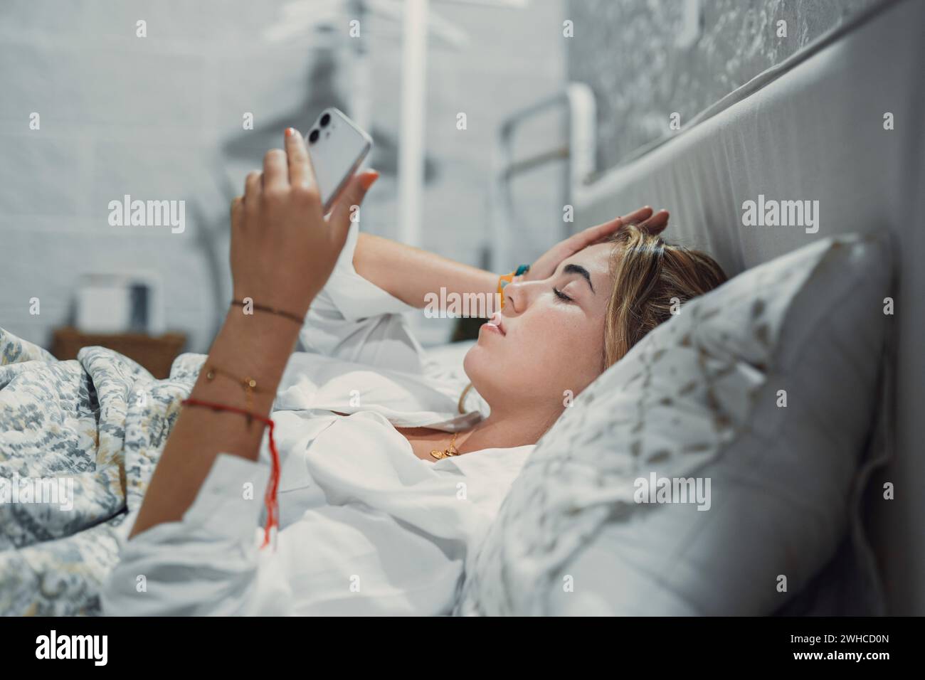 Top view unhappy woman feeling headache after sudden awakening by phone call, message signal or alarm in early morning, exhausted young female suffering from insomnia or migraine, lying in bed Stock Photo