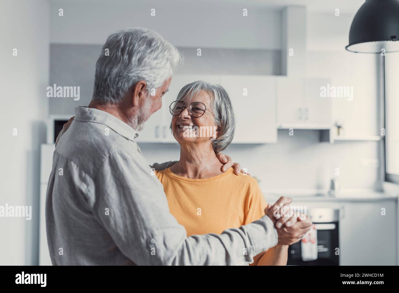 Joyful active old retired romantic couple dancing laughing in living room, happy middle aged wife and elder husband having fun at home, smiling senior family grandparents relaxing bonding together Stock Photo