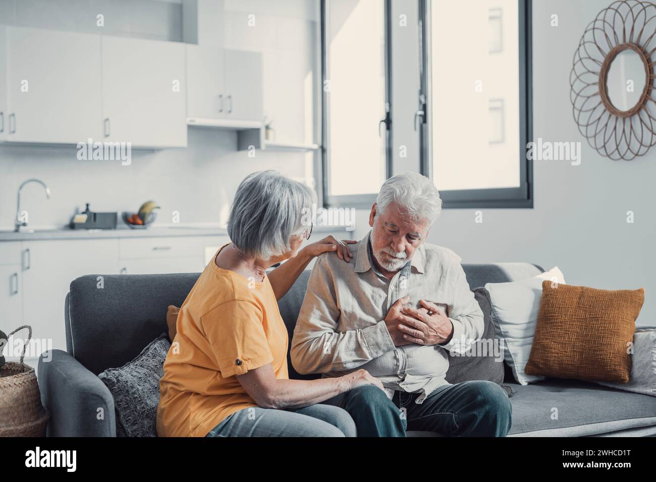 Grey haired man touching chest, having heart attack, feeling pain, suffering from heartache disease at home, mature woman supporting, embracing him, middle aged family, horizontal banner, close up Stock Photo