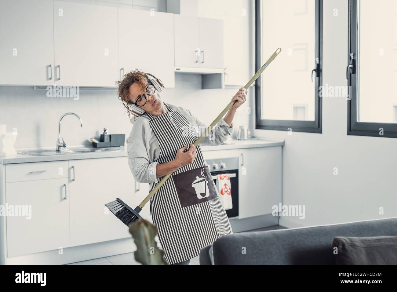 Carefree happy young woman cleaning house living room have fun dancing with mop, smiling overjoyed millennial girl feel excited enjoy making home chores sing entertain using floor broom or Swiffer Stock Photo