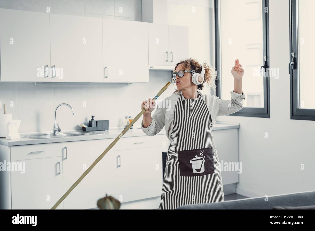 Carefree happy young woman cleaning house living room have fun dancing with mop, smiling overjoyed millennial girl feel excited enjoy making home chores sing entertain using floor broom or Swiffer Stock Photo