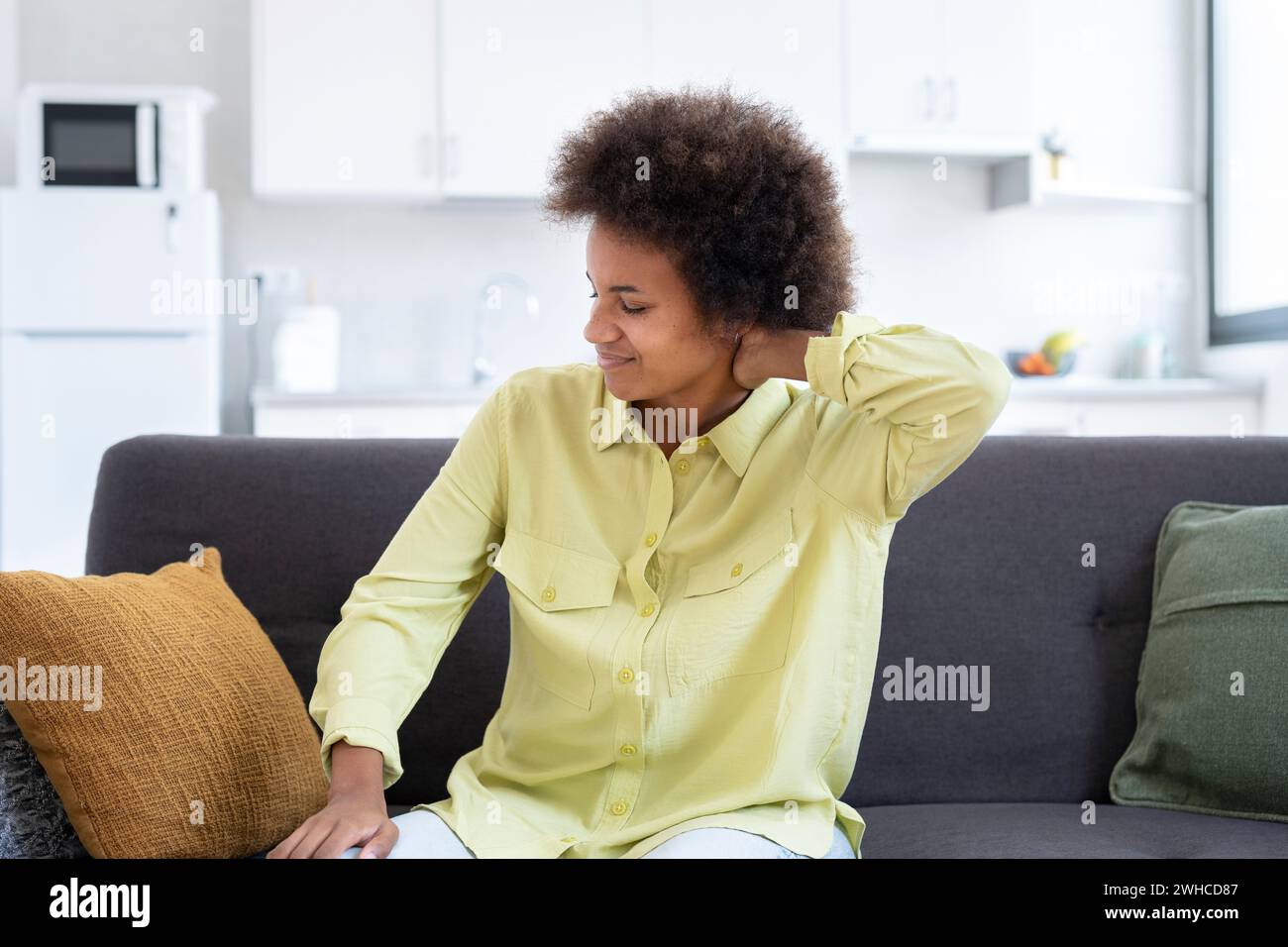 Tired upset african young woman massaging hurt stiff neck isolated on sofa at home, fatigued sad black lady rubbing tensed muscles to relieve joint shoulder pain, fibromyalgia concept Stock Photo