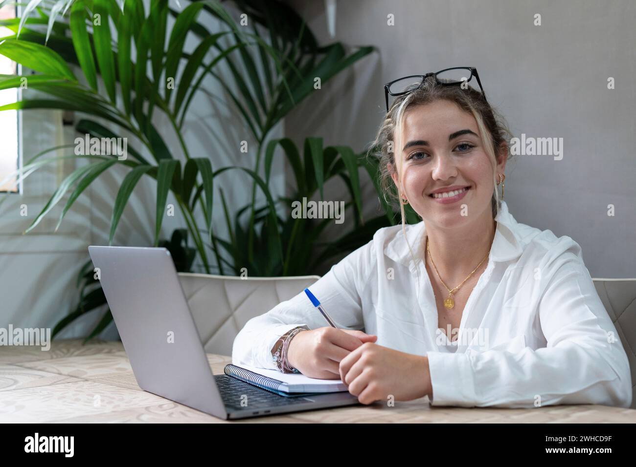 Portrait of smiling millennial caucasian female student sit at desk at home study online on laptop. Happy young cheerful woman use computer take distant course or training. Education concept. Stock Photo
