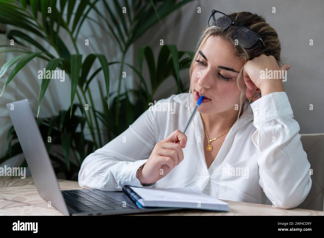 Portrait of serious millennial caucasian female student sit at desk at home study online on laptop. Thoughtful young attractive woman use computer take distant course or training. Education concept. Stock Photo