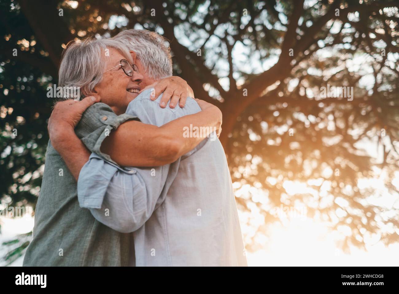 Head shot close up portrait happy grey haired middle aged woman snuggling to smiling older husband, enjoying tender moment at park. Bonding loving old family couple embracing, feeling happiness. Stock Photo