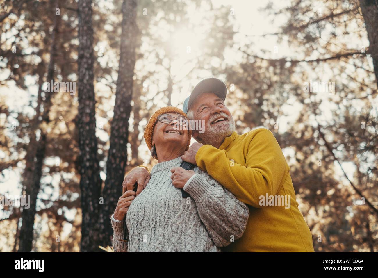 Portrait, close up of middle age cheerful people smiling and looking at the the trees of the forest around them. Active couple of old seniors hiking and walking together in the mountain having fun. Stock Photo