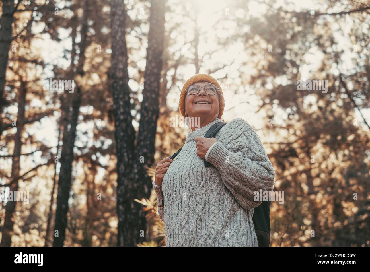 Portrait, close up of middle age caucasian woman walking and enjoying nature in the middle of trees in forest. Old mature female wearing glasses trekking and discovering. Stock Photo