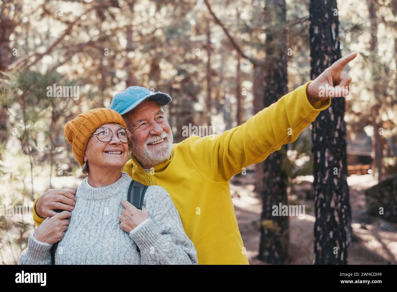 Portrait, close up of middle age cheerful people smiling and looking at the the trees of the forest around them. Active couple of old seniors hiking and walking together in the mountain having fun. Stock Photo