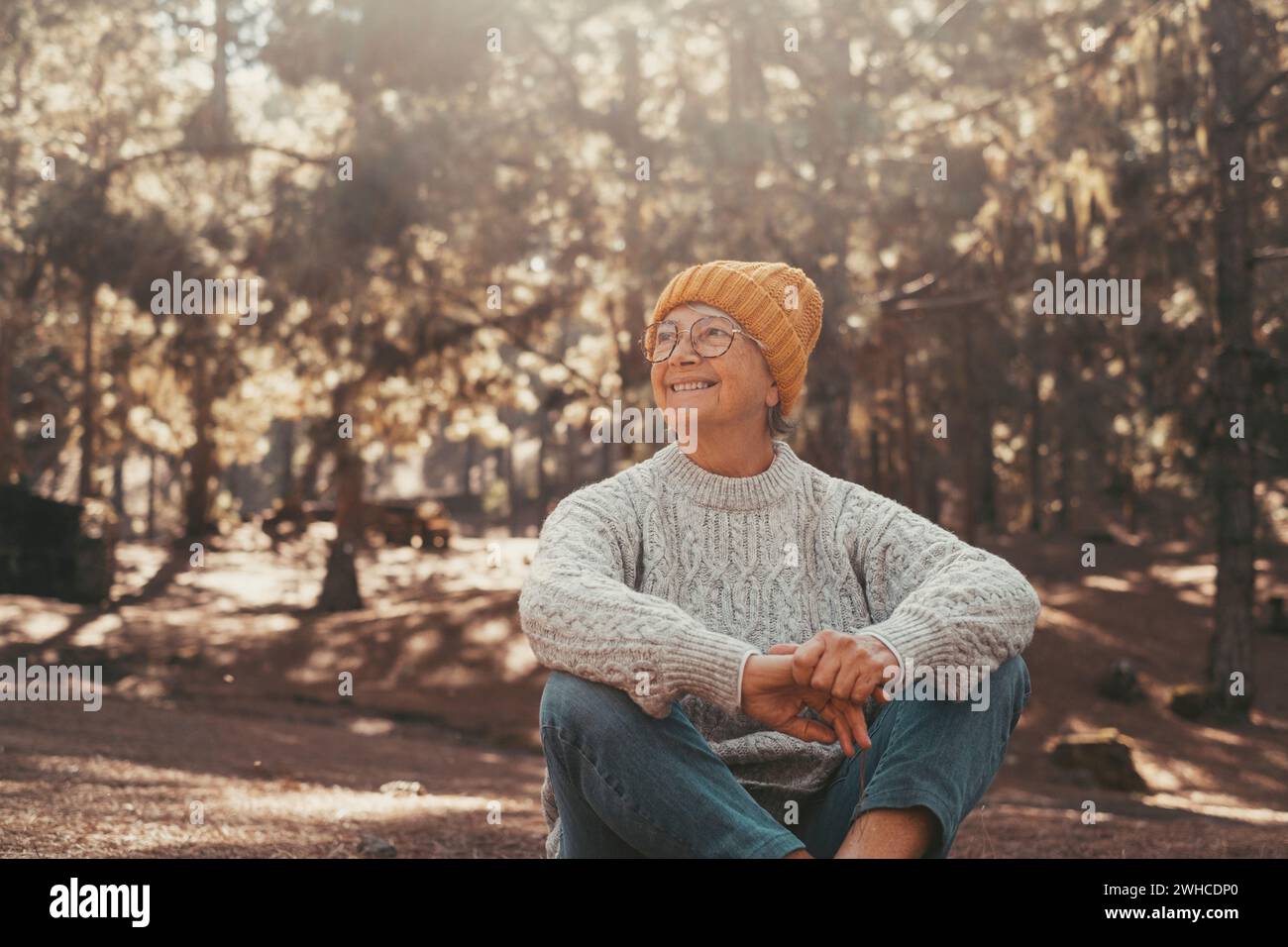 Portrait, close up of one middle age old woman resting and relaxing doing yoga in the forest of mountain in the nature. One mature cheerful female person smiling enjoying. Stock Photo