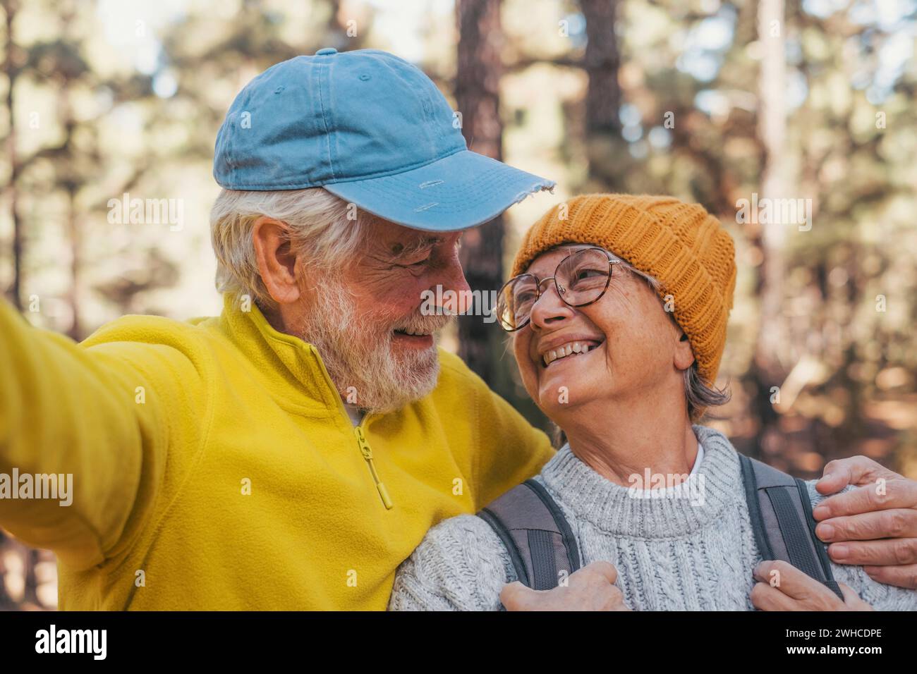 Portrait, close up of cute couple of old seniors taking a selfie together in the mountain forest looking at the camera smiling having fun enjoying. Two mature people hiking. Stock Photo