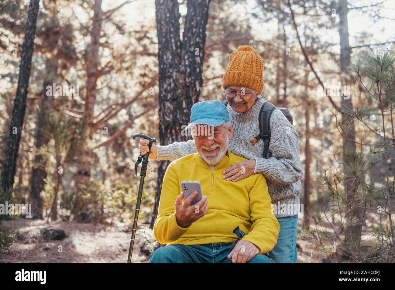 Portrait, close up of couple of cute seniors using phone together in the forest with trees around them. Using cellphone mobile outdoors having fun and enjoying. Stock Photo