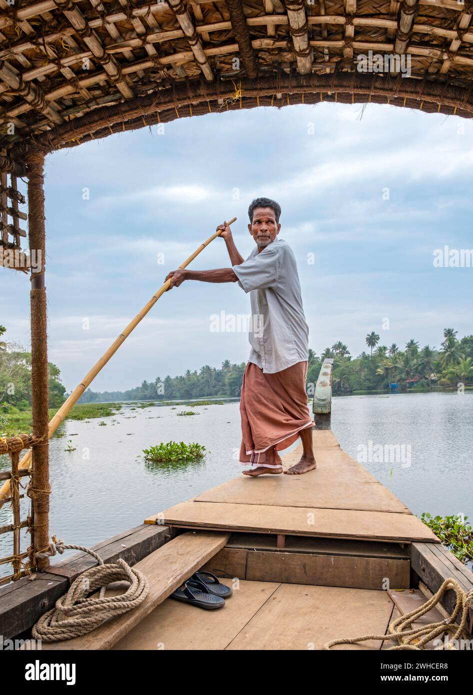 A man navigates a boat through the canals of the Kerala Backwaters using a long pole, Vembanad Lake, Kerala, India Stock Photo