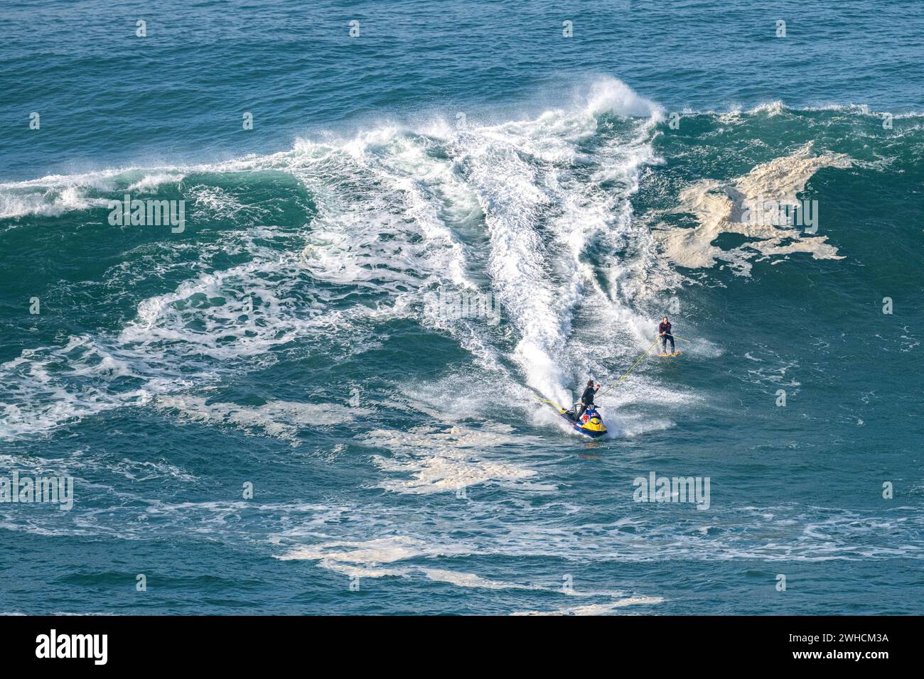 A jet ski and a water skier with poles on a big wave, Nazaré, Portugal