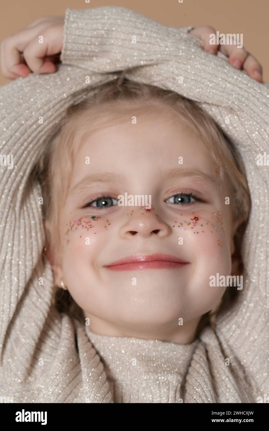 Portrait of cute little blonde girl with blue eyes and glitters on her face. Stock Photo