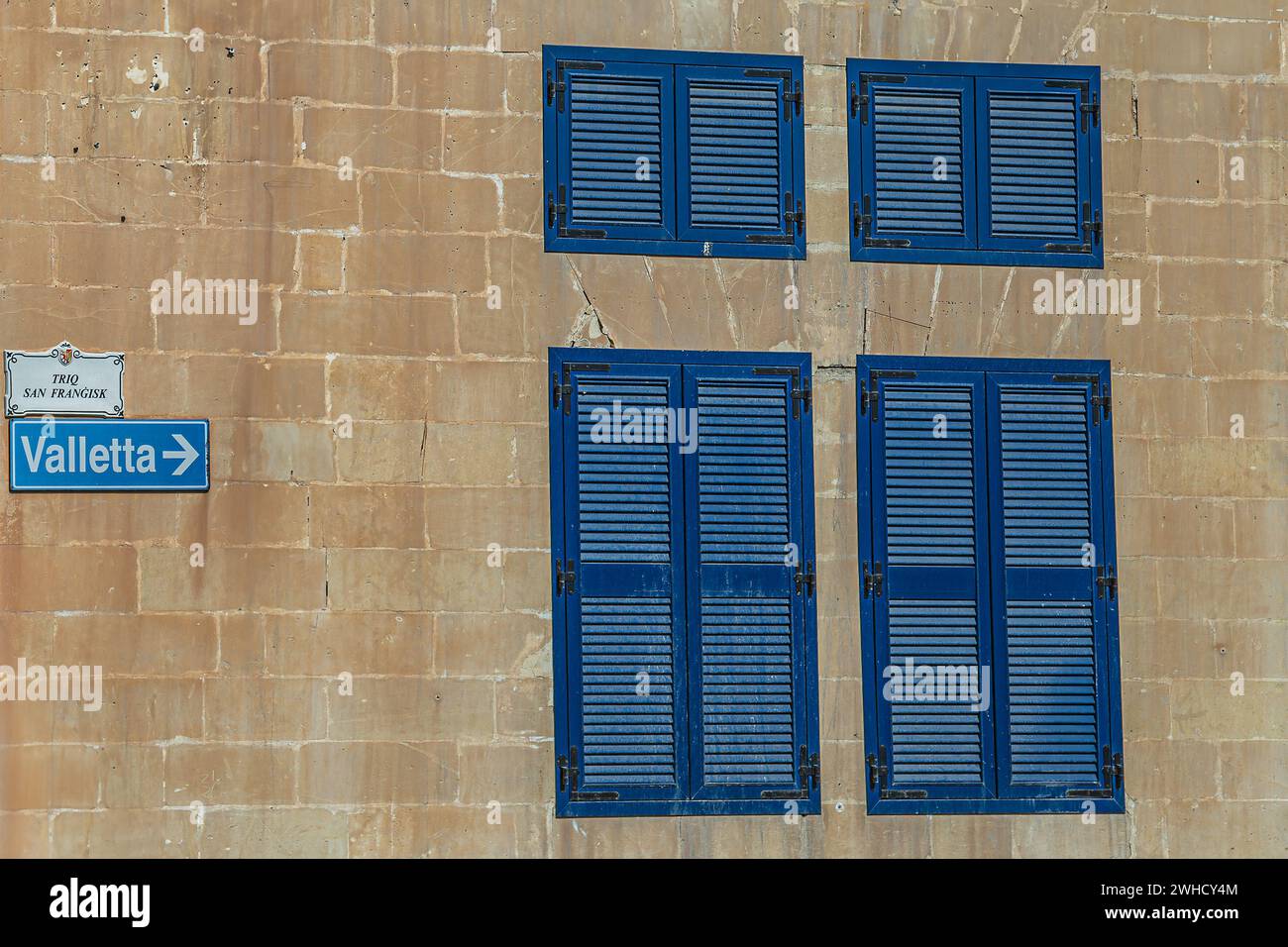 Maltese minimalist architecture. Wall made of locally specific limestone bricks and window shutters traditionally colored in blue. Street signs and di Stock Photo