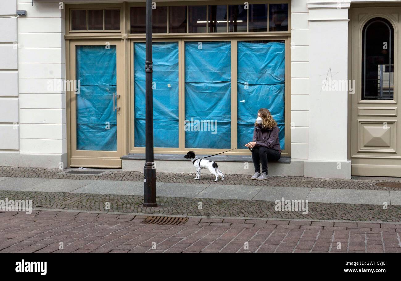 A woman sits with her dog in front of a closed shop. Customers who want ...