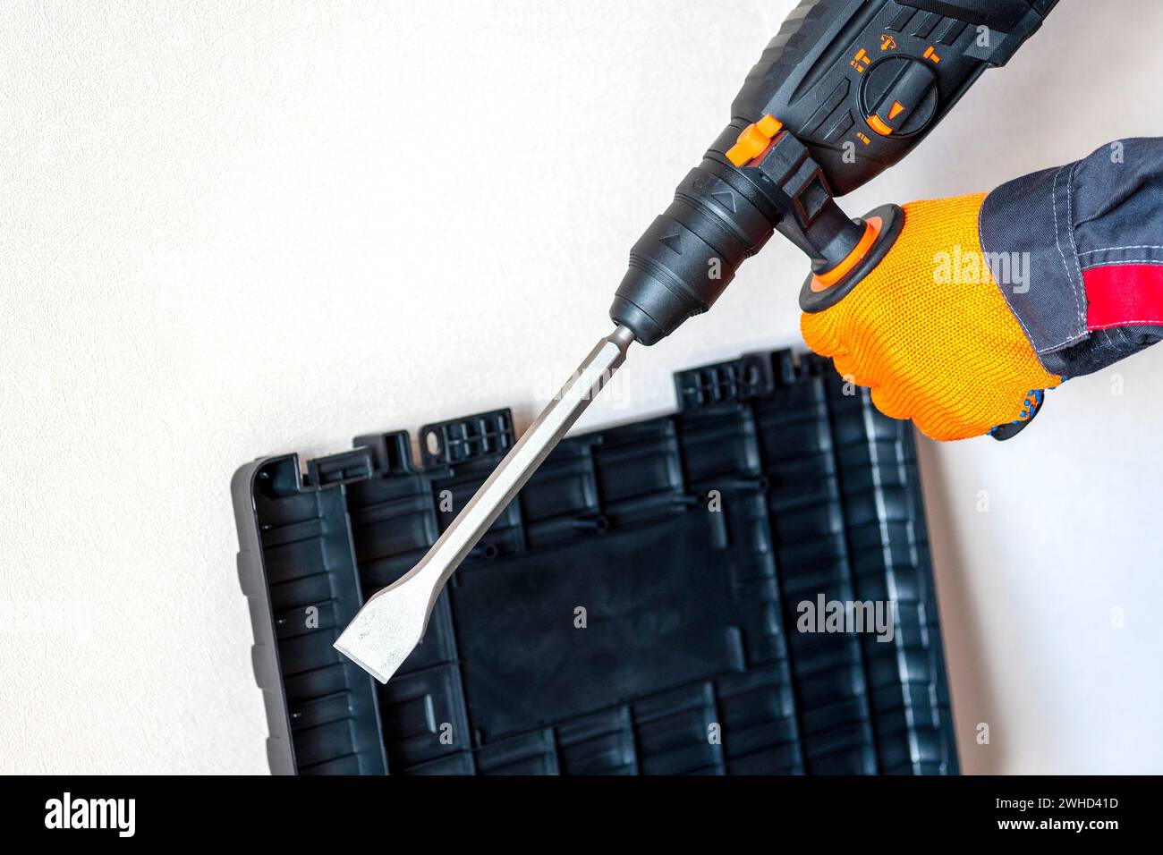 workman with a rotary hammer. Hands in protective gloves with hammer drill perforator. Copy space. Stock Photo