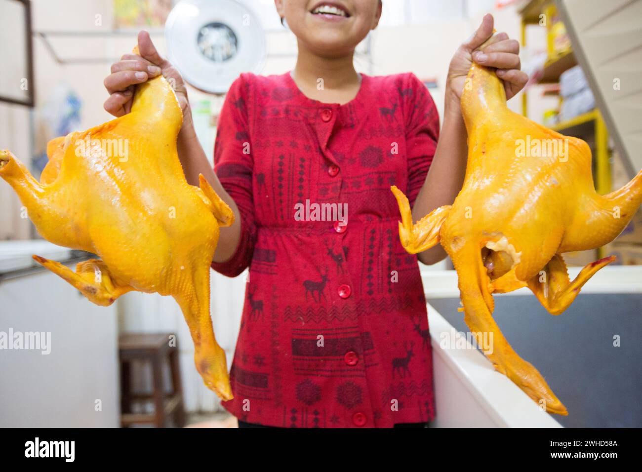 Tupiza, Bolivia - 30th December 2014: Young Asian girl smiling and holding two chickens on sale inside a local shop in Tupiza, Bolivia Stock Photo