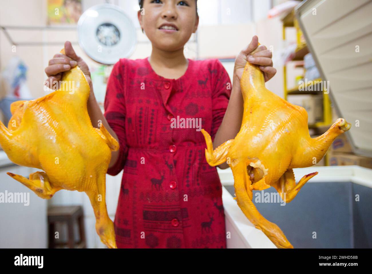 Tupiza, Bolivia - 30th December 2014: Young Asian girl smiling and holding two chickens on sale inside a local shop in Tupiza, Bolivia Stock Photo
