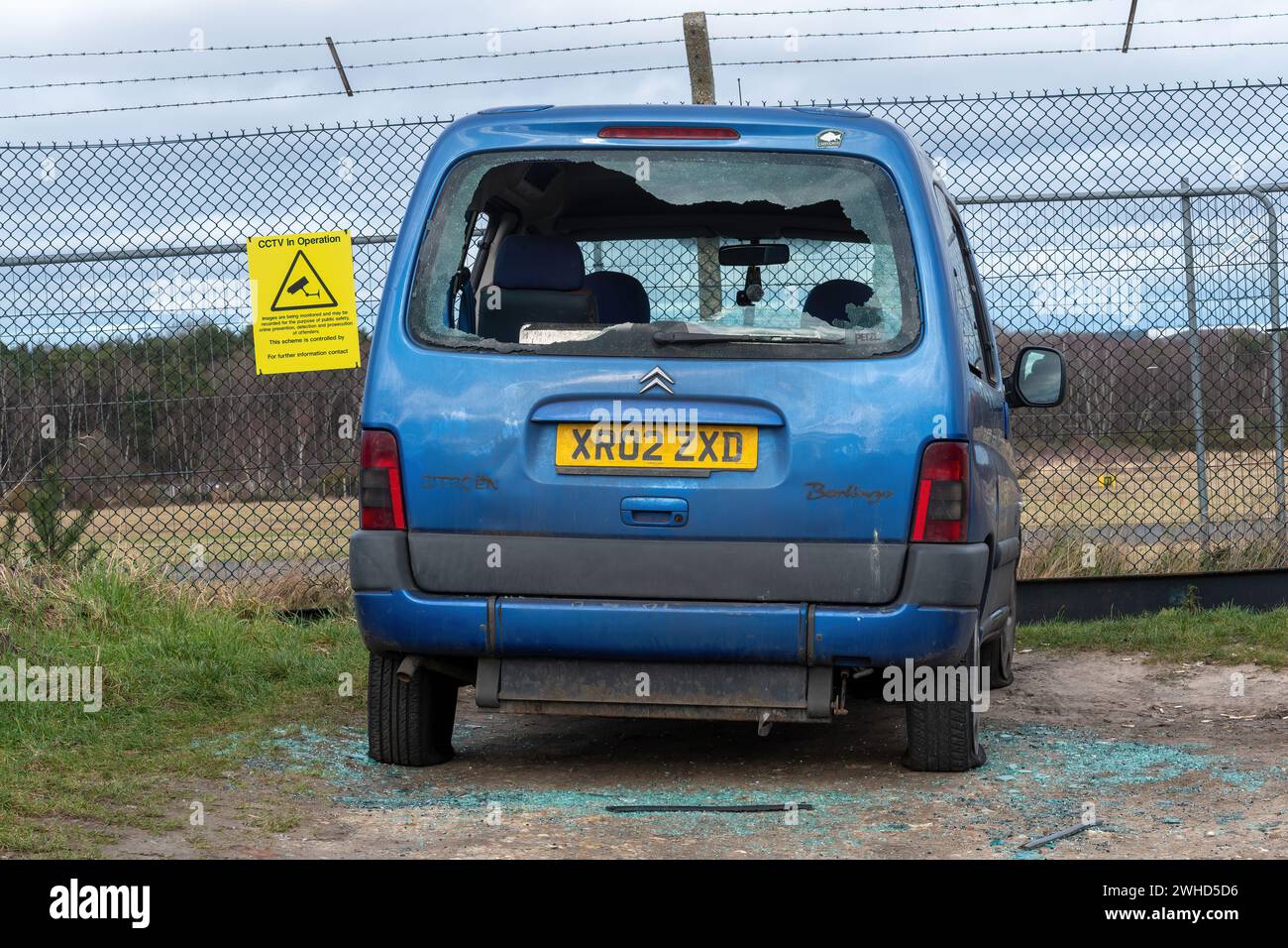 Car crime concept: a car with a smashed rear windscreen despite being parked next to a sign about CCTV in Operation cameras Stock Photo