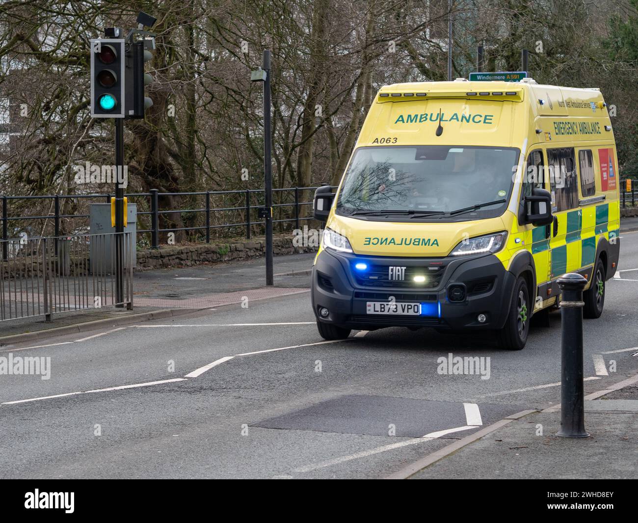 An speeding ambulance with blue lights flashing crosses a pelican pedestrian crossing down Sandes Avenue in Kendal, Cumbria, UK on an emergency call. Stock Photo