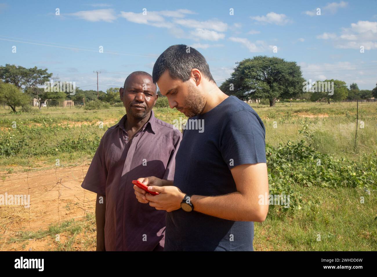 african village, old entrepreneur man together with a ngo social worker using a phone learning new skills for a small business Stock Photo