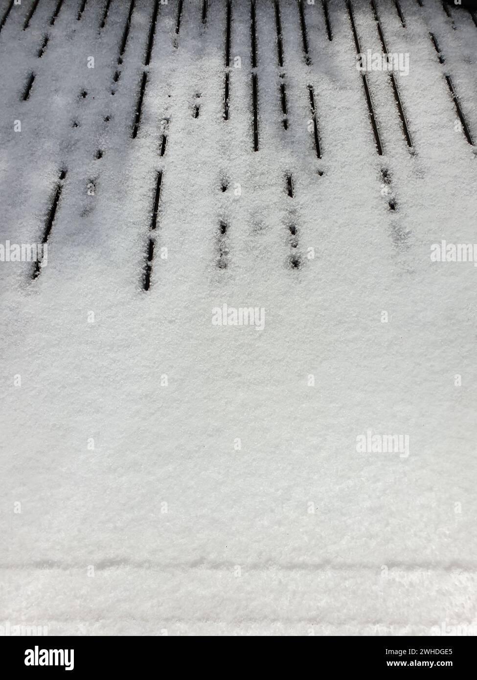 View through the window of the weather phenomenon in May in Berlin with sunshine on the wooden floor of the terrace forming a kind of keyboard in the snow Stock Photo