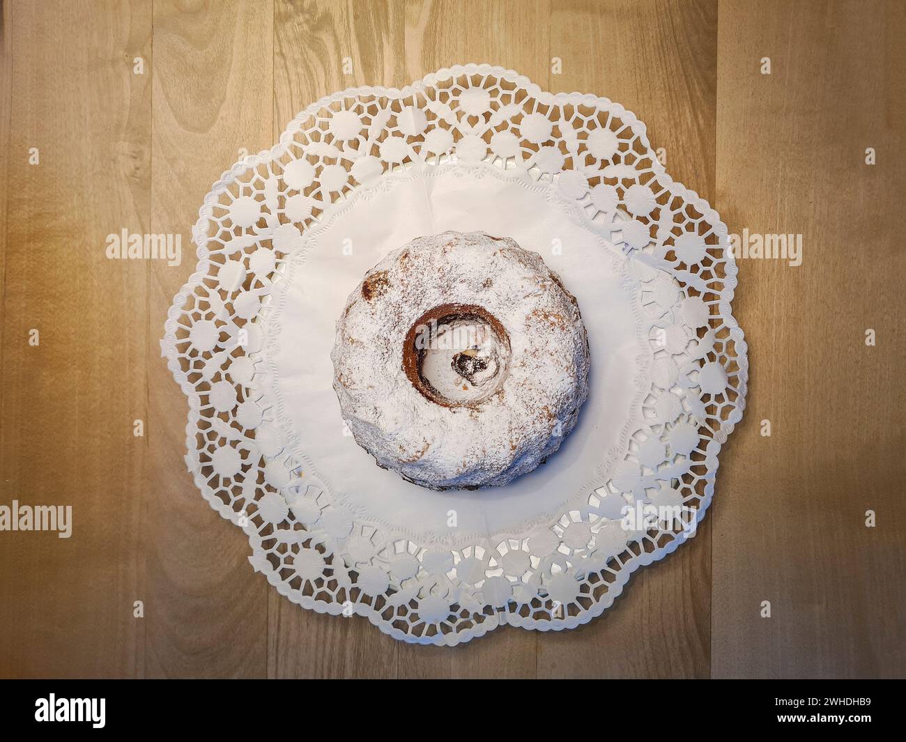 Round marble cake with powdered sugar and crumbs on a white paper tablecloth as decoration on a wooden table Stock Photo