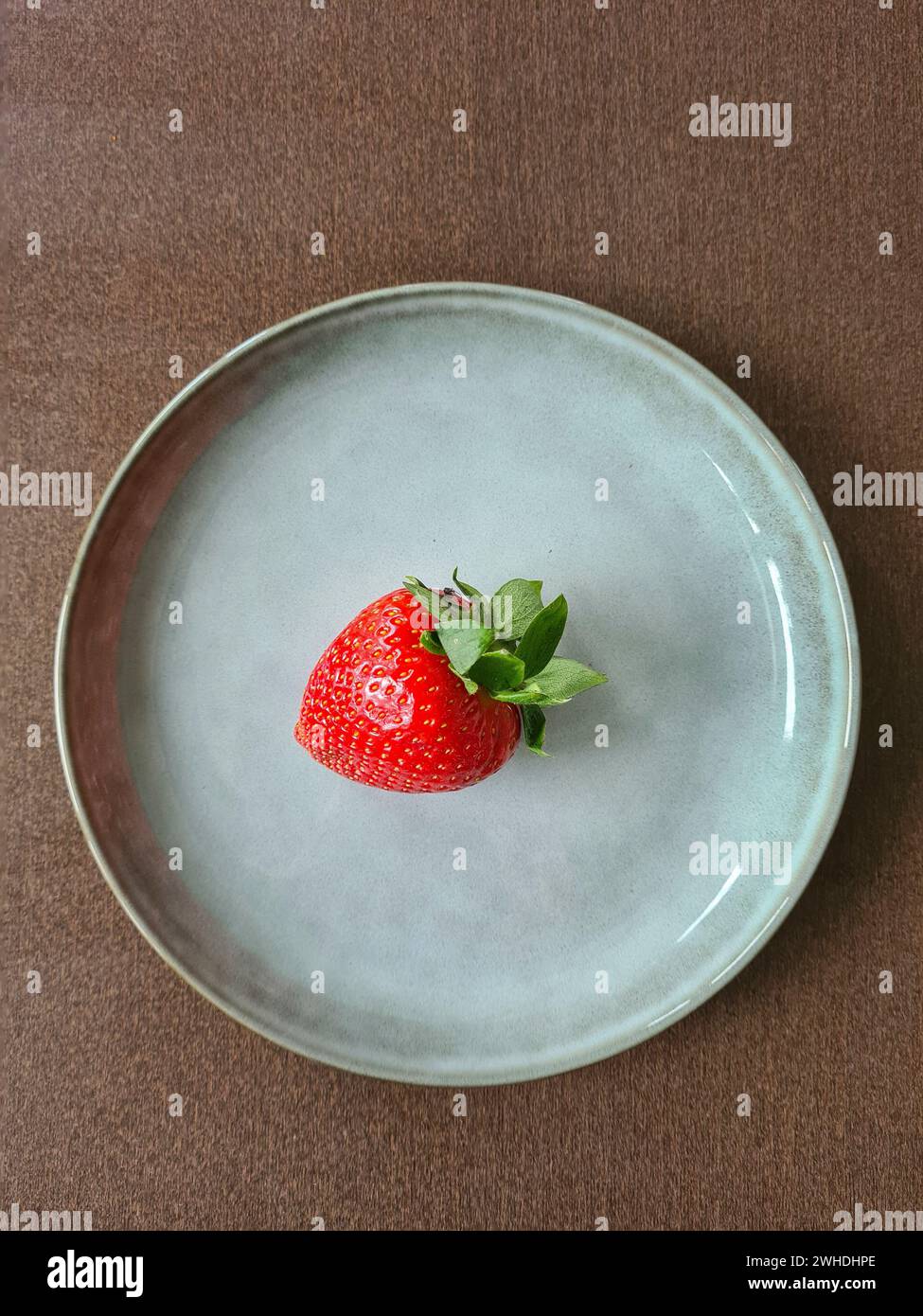 A fresh red ripe strawberry with green on a plate Stock Photo