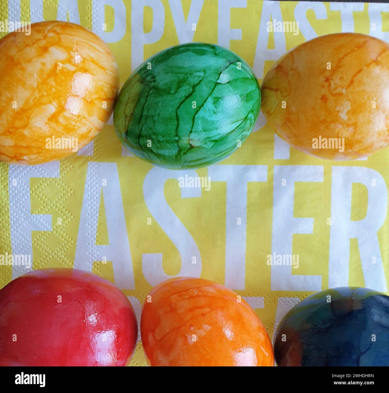 Boiled colorful eggs in the egg colors yellow green blue and red lie on a yellow napkin with white lettering for Easter Stock Photo