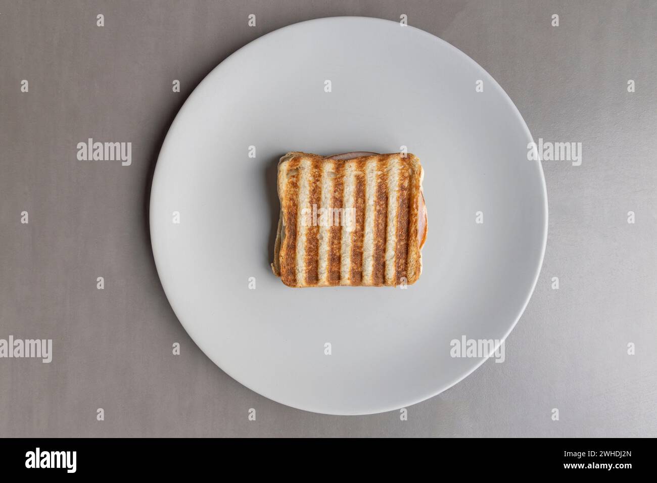 A grilled ham toast sandwich with a striped pattern lies on a light gray plate against a gray background Stock Photo