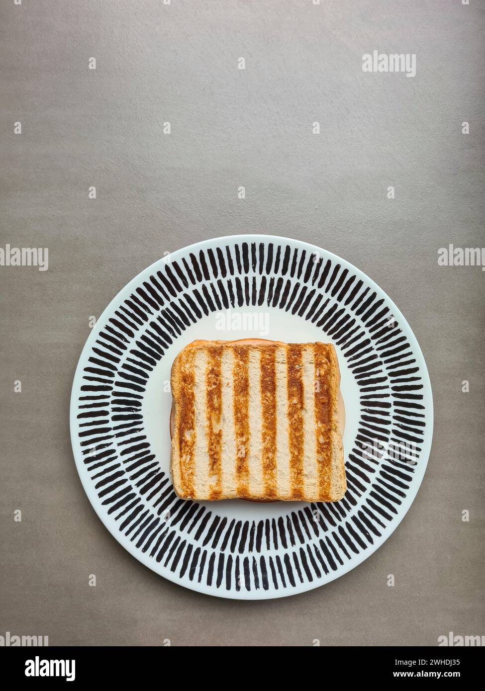 A grilled ham toast sandwich with a striped pattern lies on a plate against a gray background Stock Photo