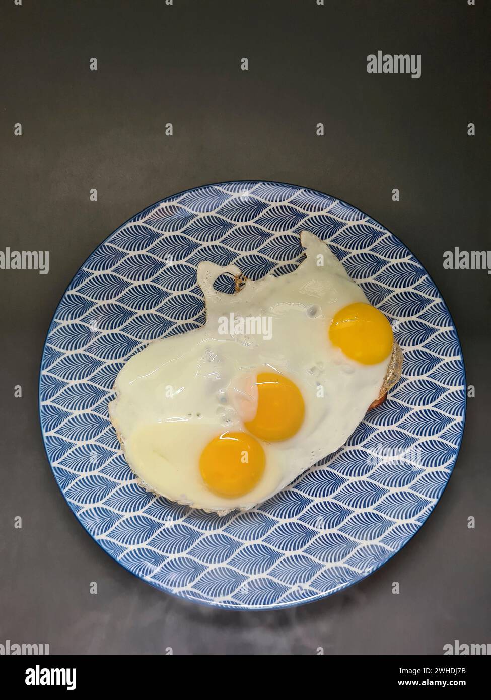 three fried eggs on a blue and white plate Stock Photo