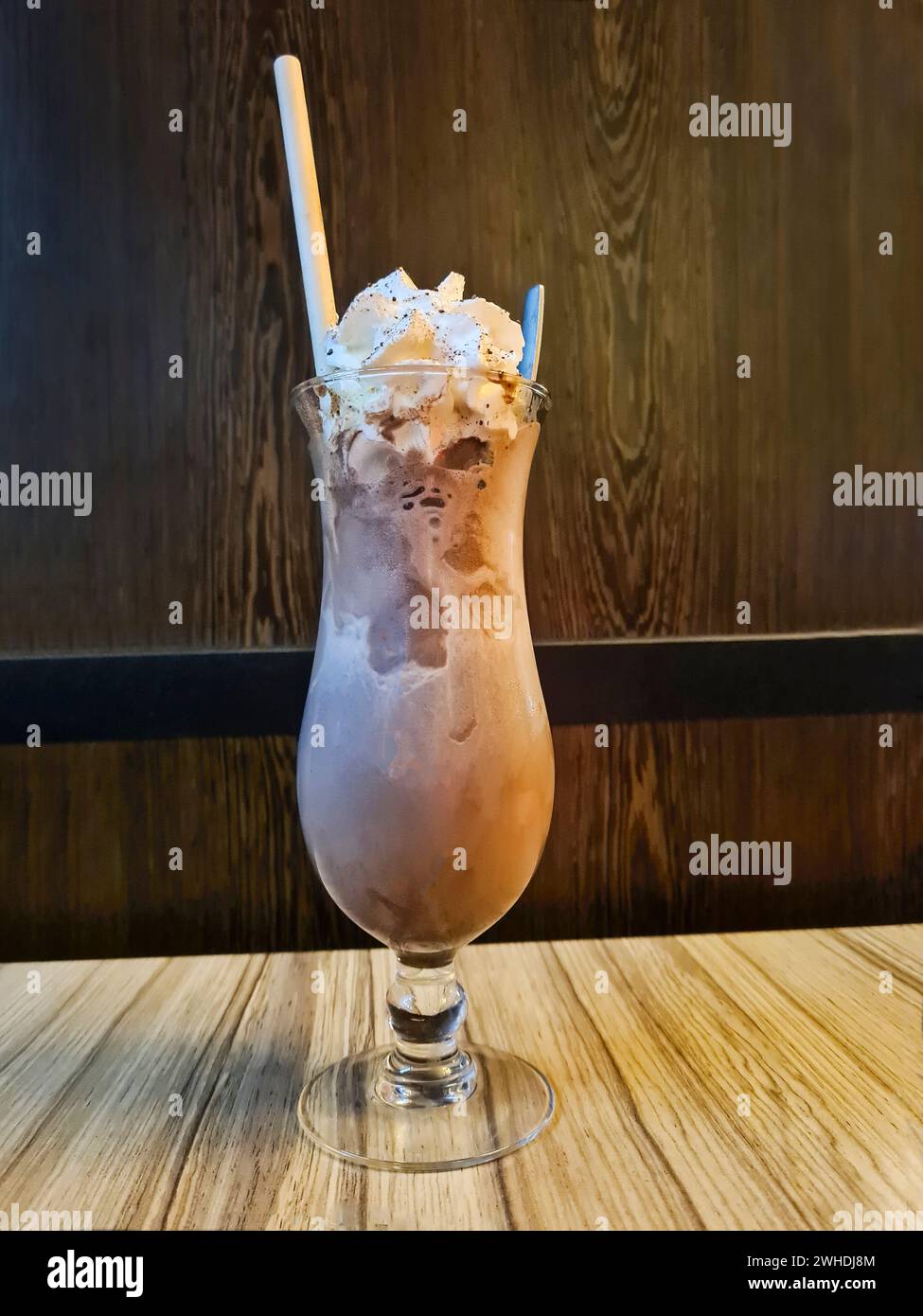 Ice chocolate with cream in a tall glass with a straw and spoon is stylishly arranged on a table in the restaurant Stock Photo