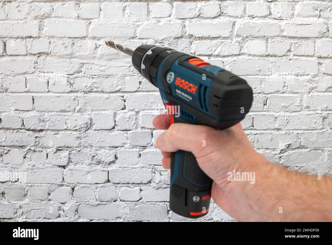 Man's hand holding Bosch cordless drill, with inserted masonry drill
