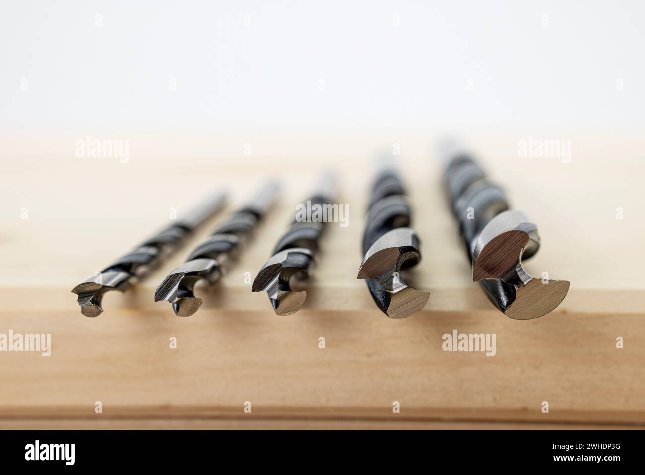 Woodworking, five wood twist drills 4, 5, 6, 8 and 10 mm, lying on glued wood panel, blurring, Stock Photo