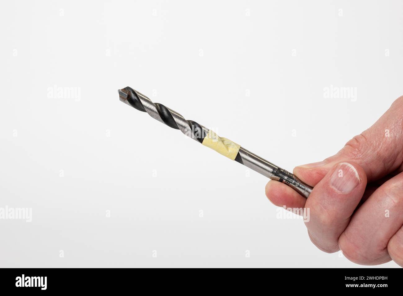 Man's hand holding a 10 mm masonry drill wrapped in masking tape