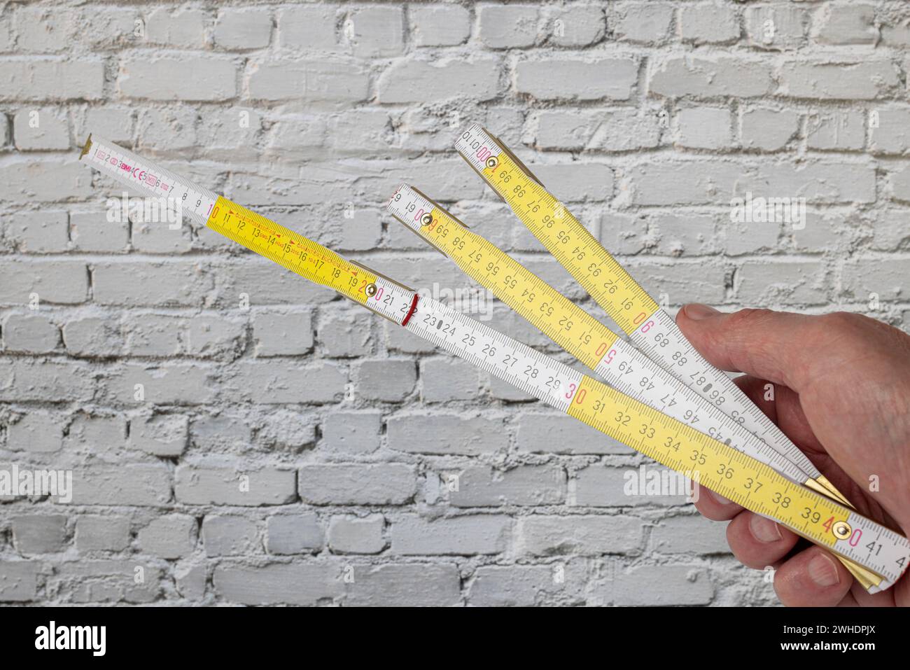 Male hand holding folding rule with millimeter and centimeter graduation, unfolded, lengths measuring tool, background white brick wall, Stock Photo